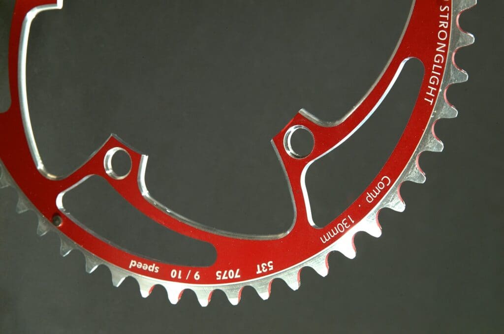 A red and silver bicycle chain ring with two holes.